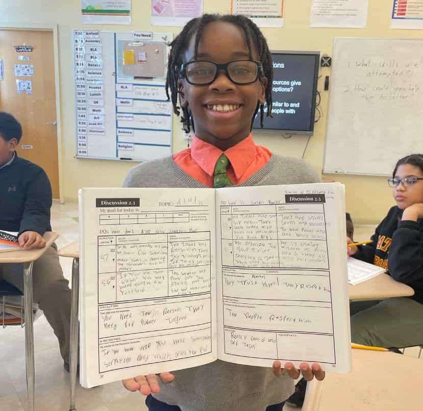 A Nativity Prep sixth grader holding up his Discussion Portfolio